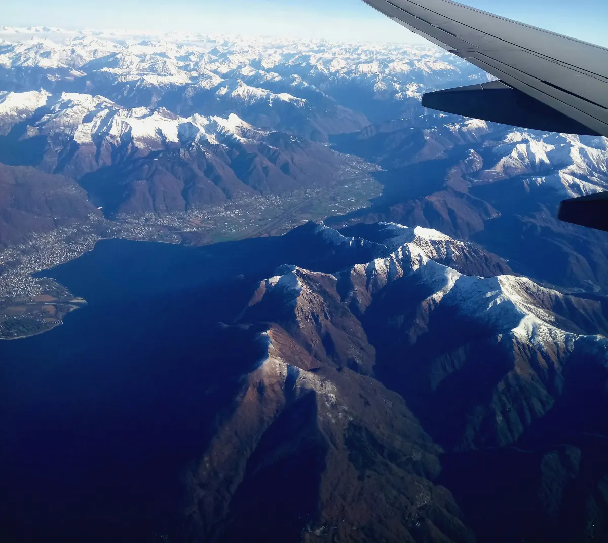 View from an airplane window over snow-capped mountains and a lake